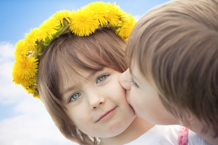 15331382-young-boy-kissing-cute-preschool-sister-with-yellow-daisy-flower-crown-blue-sky-and-cloudscape-backg.jpg